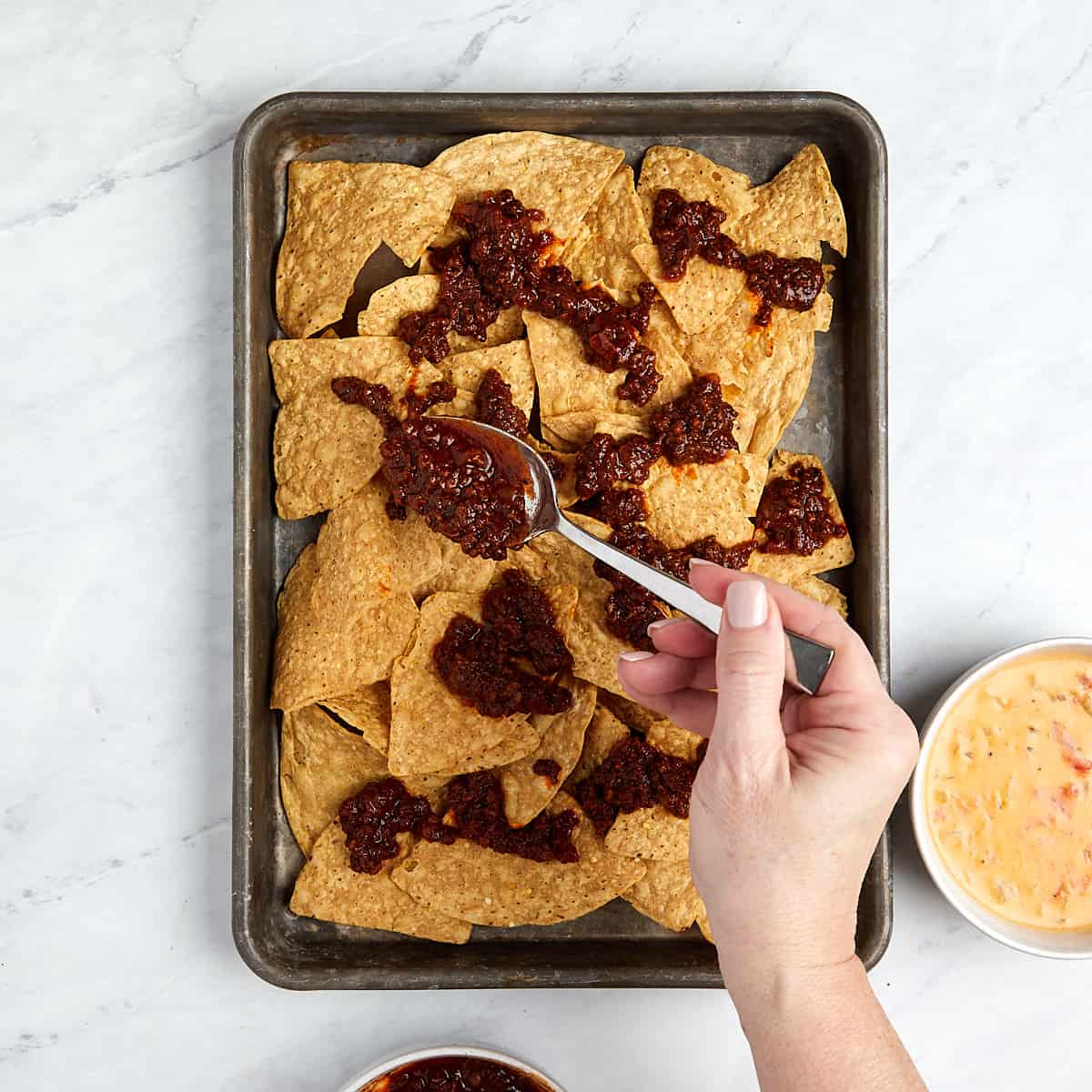 tortilla chips on a cookie sheet being topped with chili.
