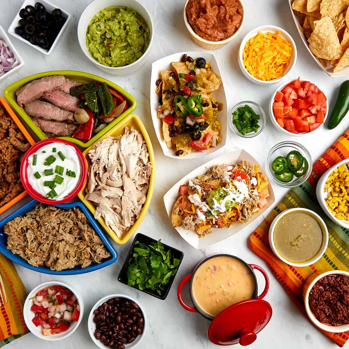 nacho bar toppings in serving containers and two servings of nachos topped with toppings