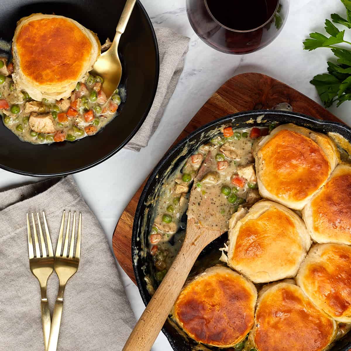 chicken pot pie being served in a black bowl with a glass of red wine.