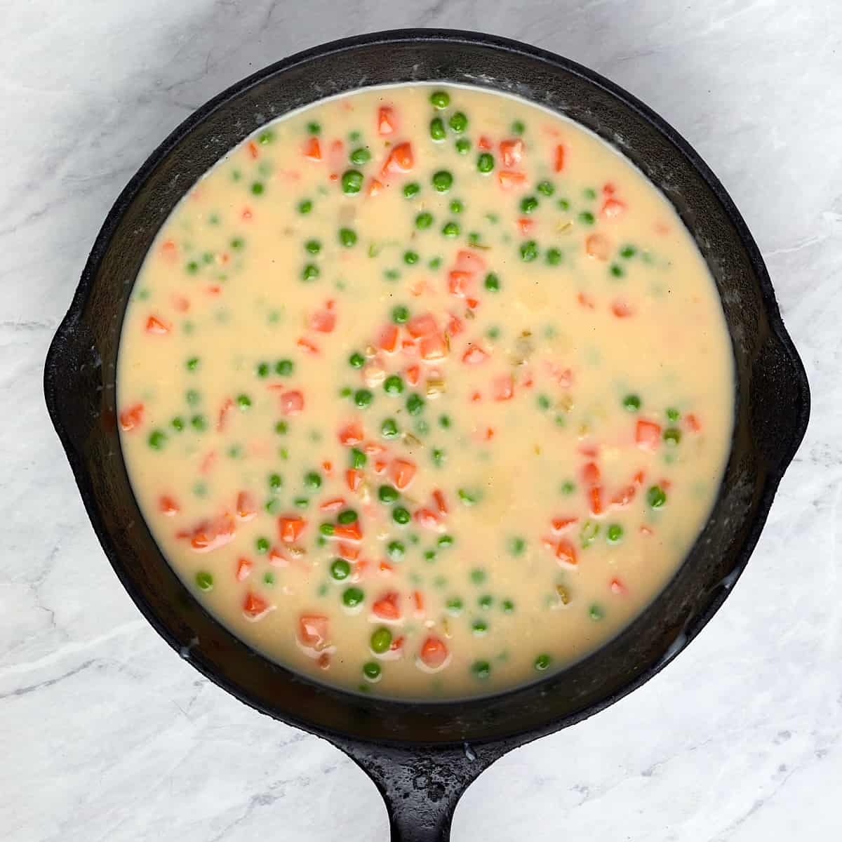 cream of celery soup, veggies, and broth cooking in a cast iron skillet.