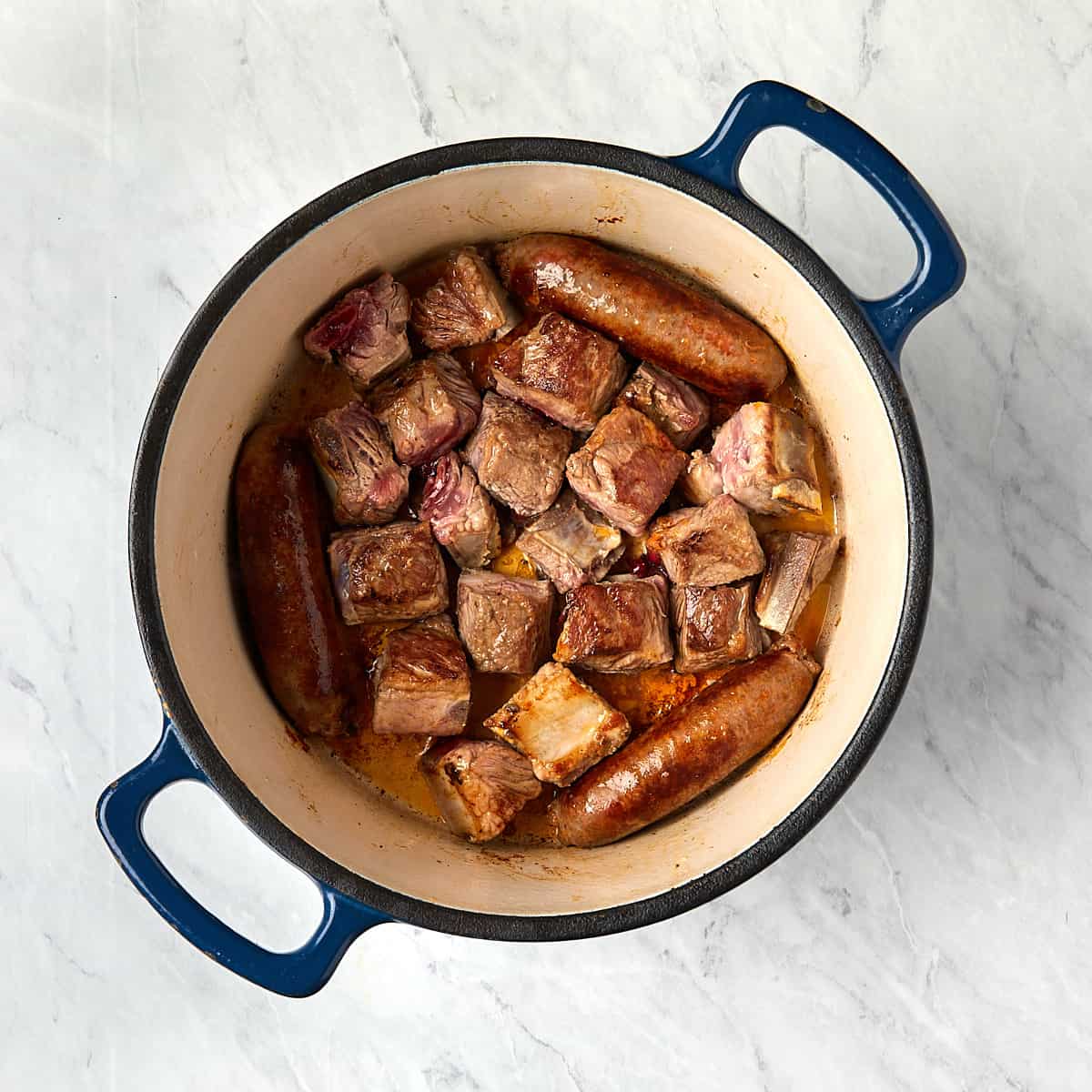 sausage and pork tips cooking in a dutch oven.