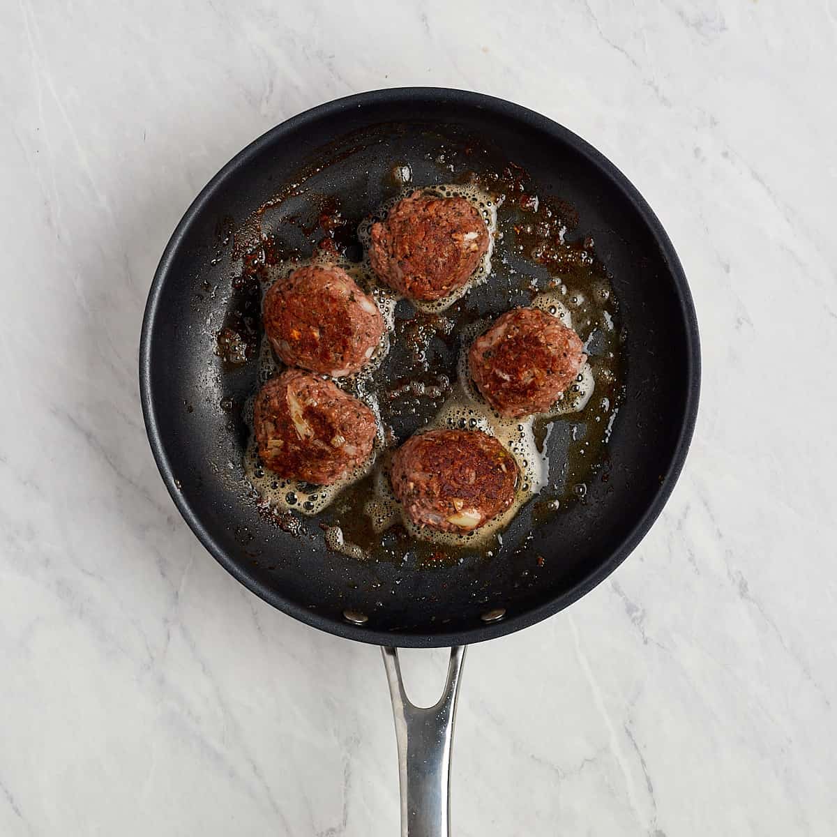 vegetarian meatballs being cooked in a non stick skillet. one side has already been browned.