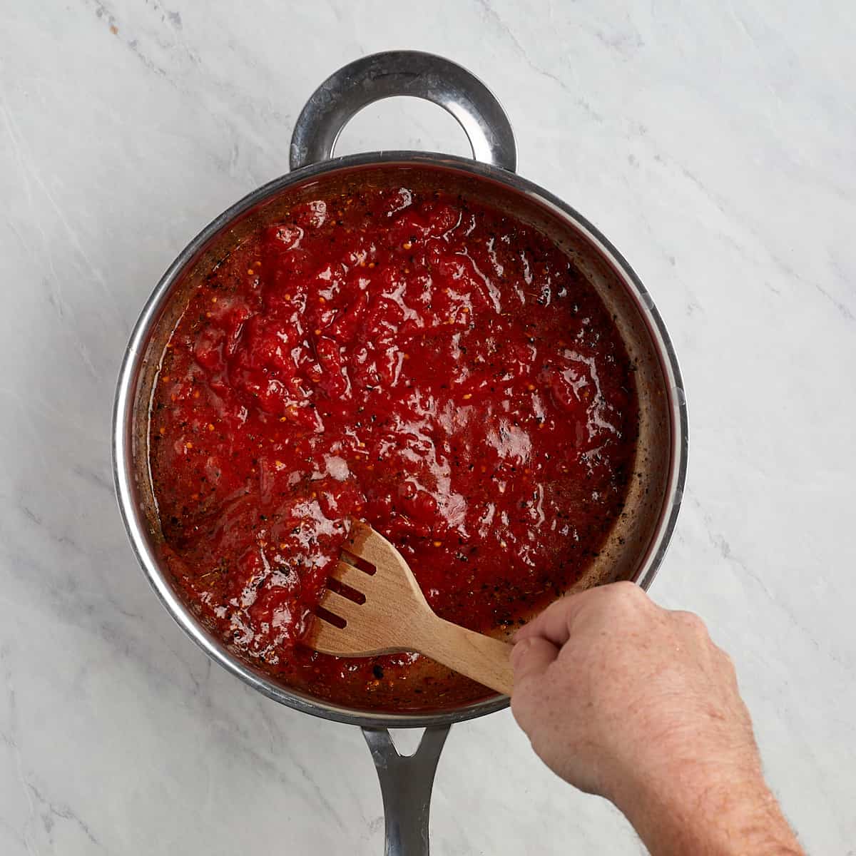 tomatoes in a skillet with the olive oil and spices being stirred with a wooden spoon.