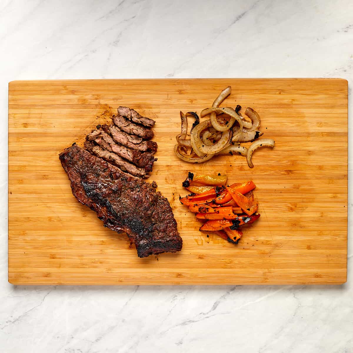 cooked skirt steak, onions, and peppers on a cutting board