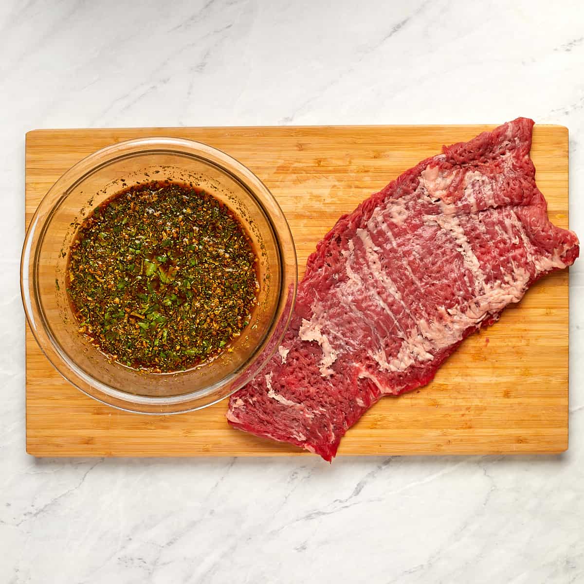 tenderized skirt steak on a cutting board and a bowl of the prepared marinade