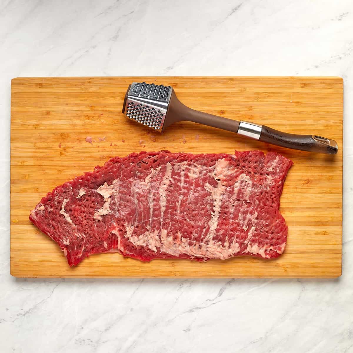 skirt steak on a cutting board with a meat mallet after being tenderized.