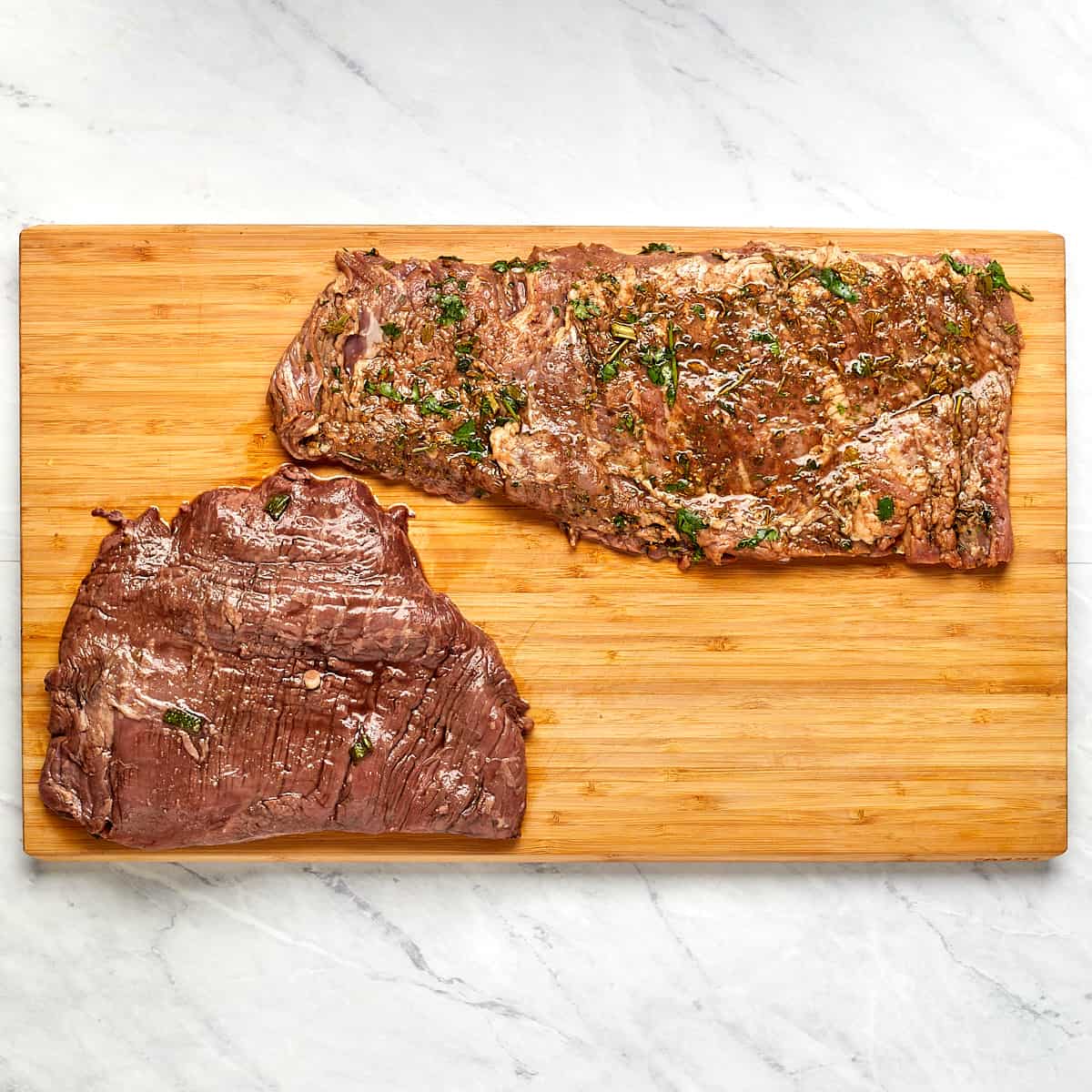 uncooked marinated flank steak and skirt steak on a wood cutting board