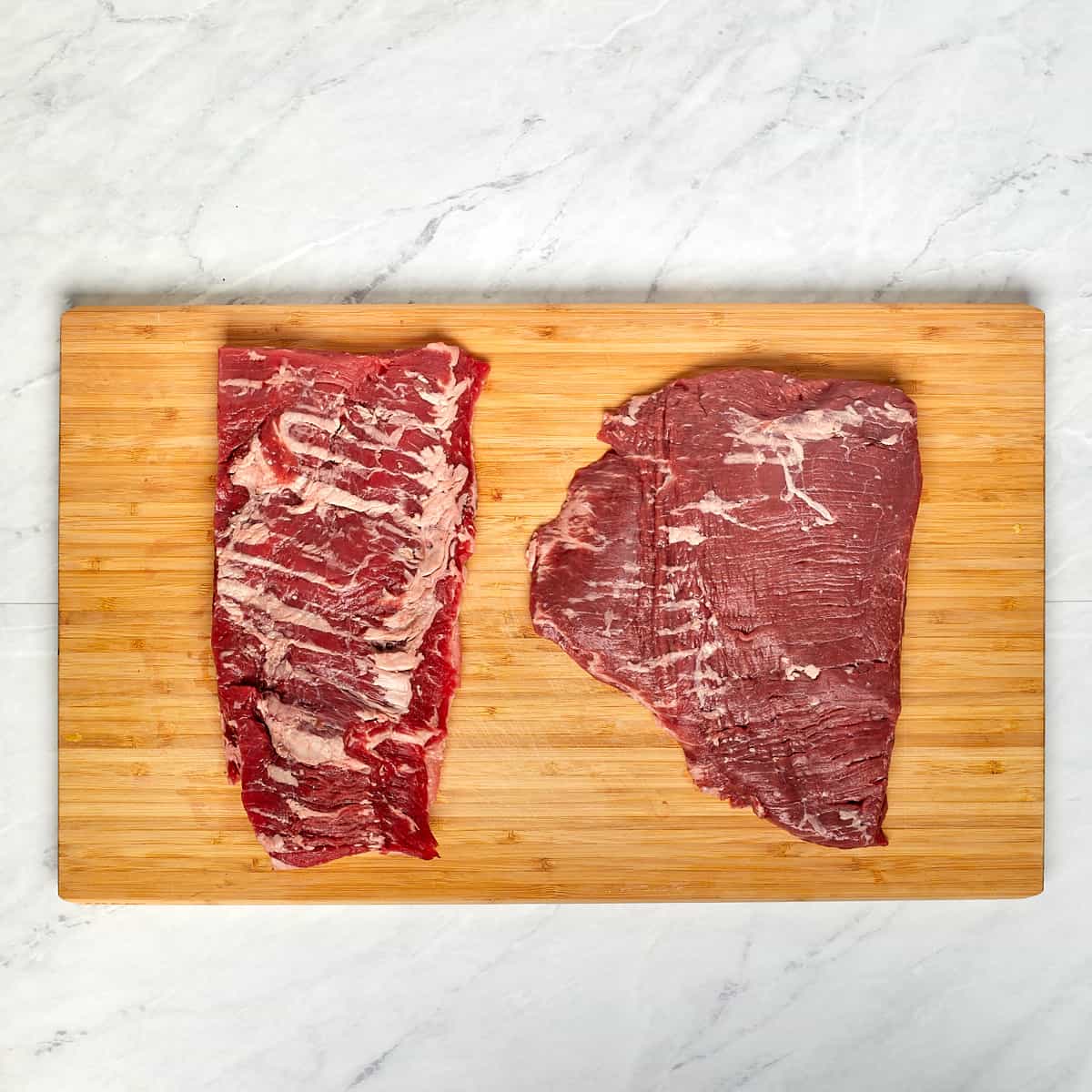 uncooked steak and skirt steak on a wood cutting board