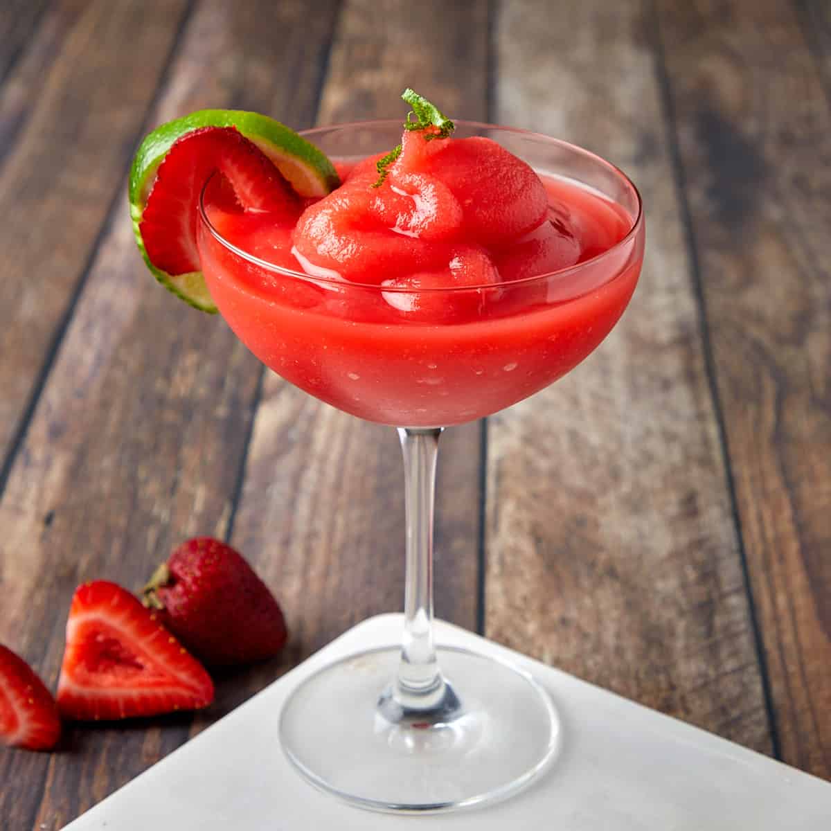 frozen strawberry daiquiri in a glass garnished with lime zest and strawberry slice
