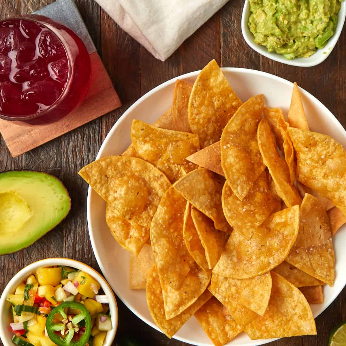 tortilla chips in a bowl with a side of guacamole and mango salsa along with a margarita on the rocks.