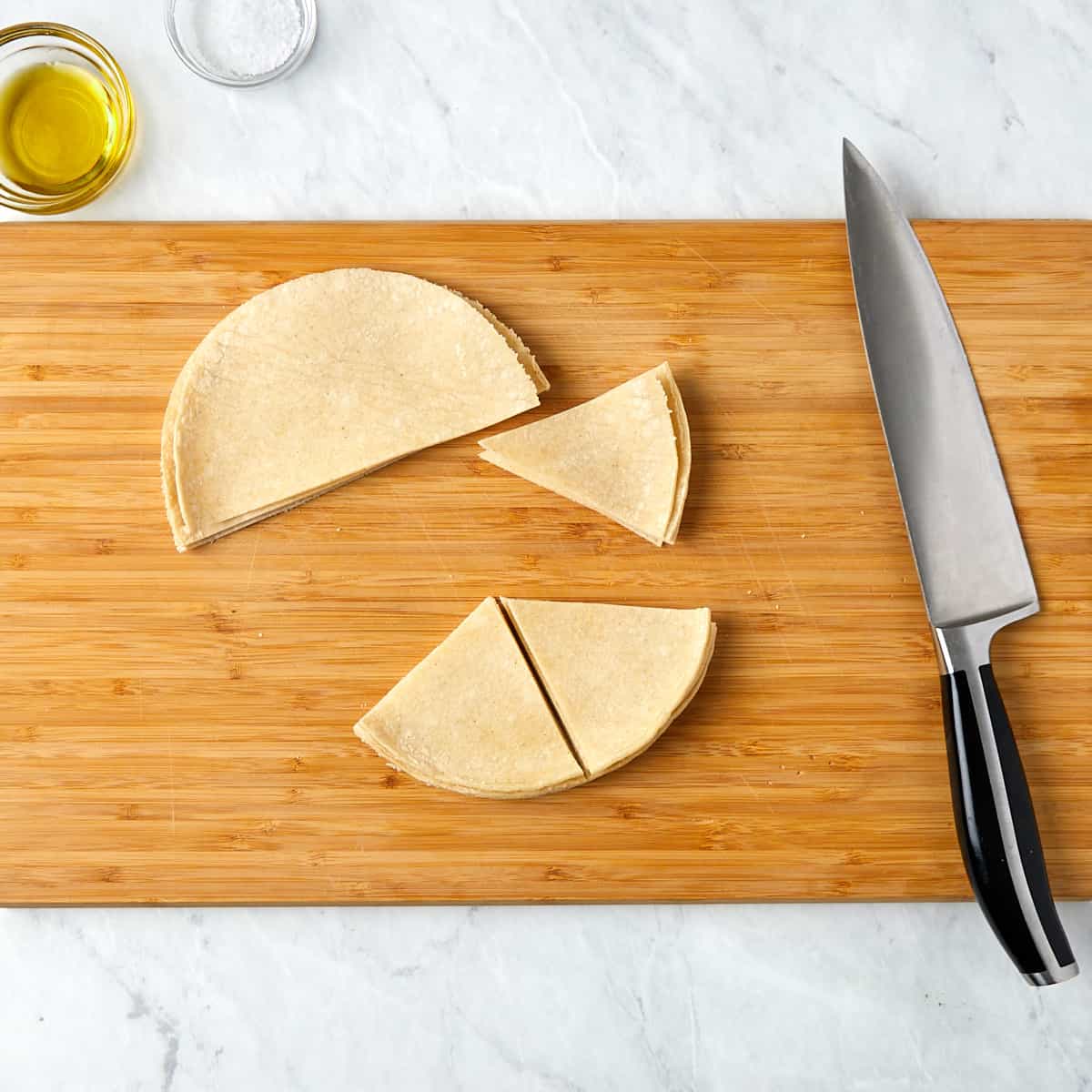 tortillas being cut into 6 triangular wedges on a wooden cutting board.