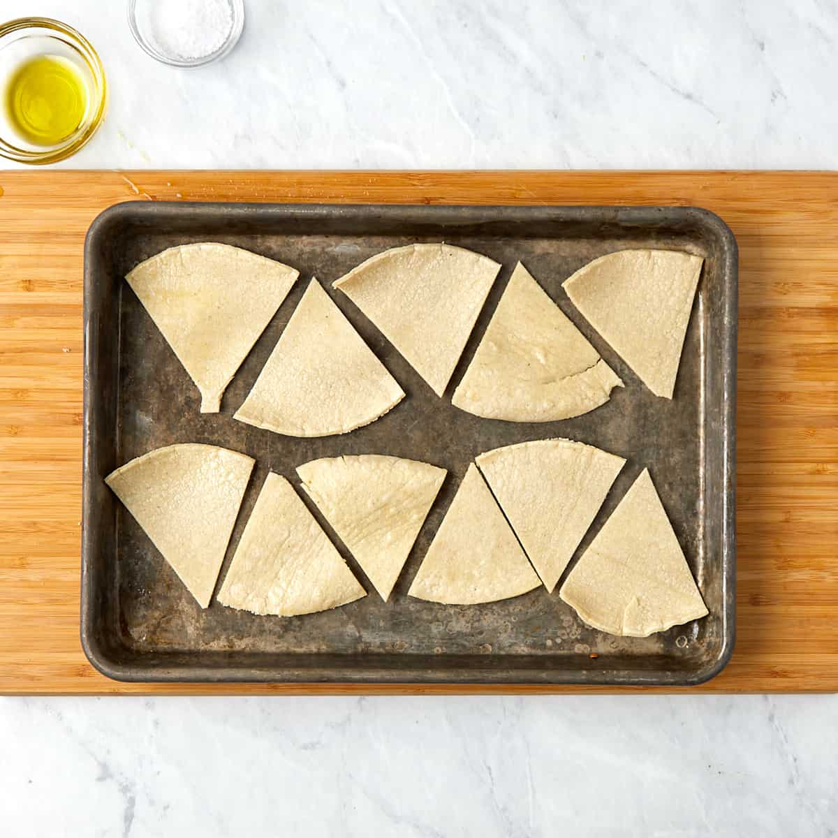 tortilla triangular wedges laid out on a baking sheet before going in the oven.