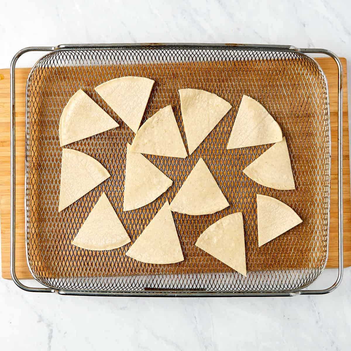 tortilla triangular wedges laid out on an air fryer tray before going in the oven.