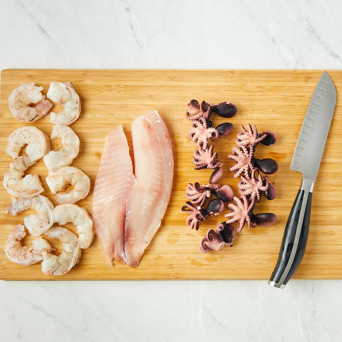 cooked baby octopus, raw tilapia, and raw shrimp on a wooden cutting board