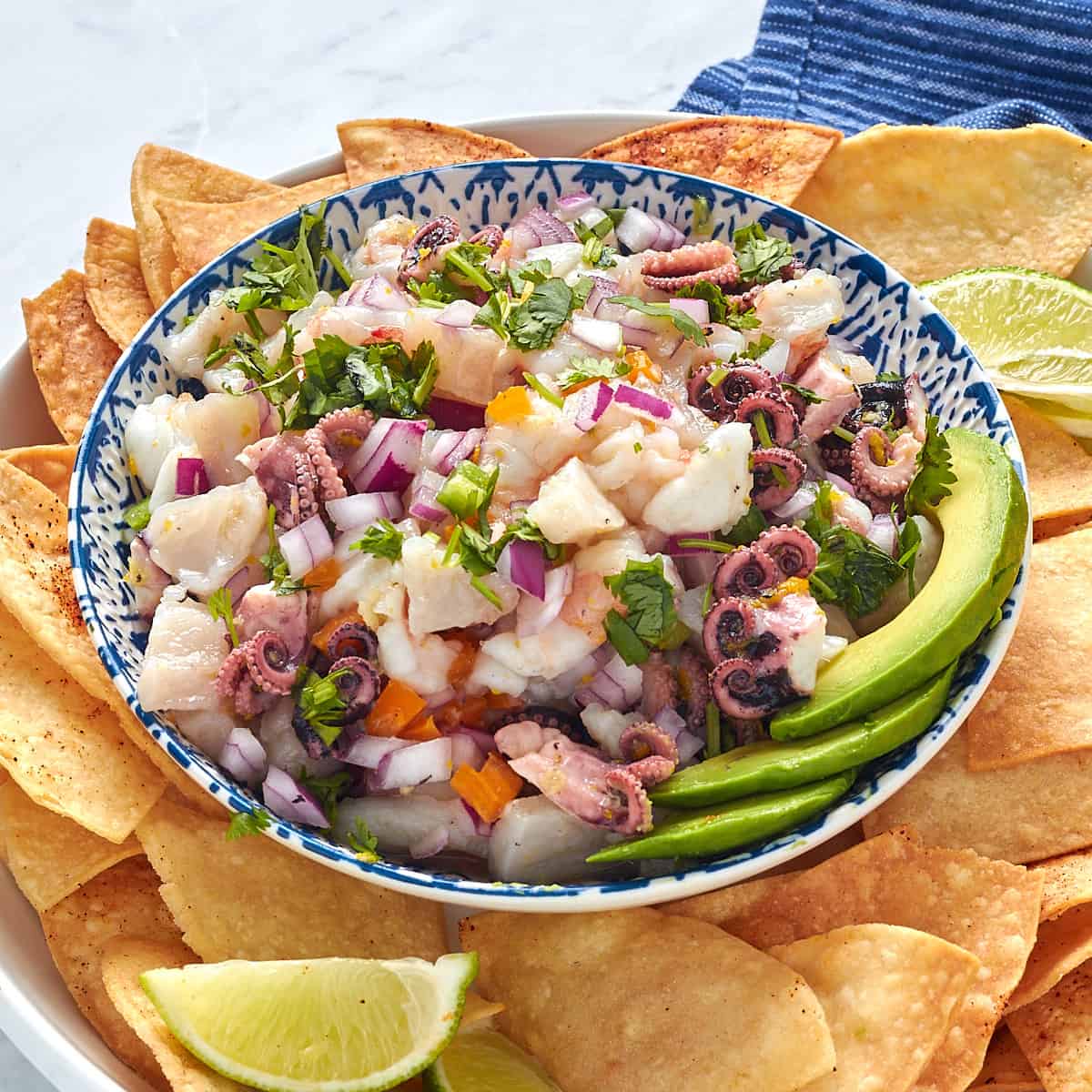 octopus ceviche in a bowl surrounded by chips and a side of avocado