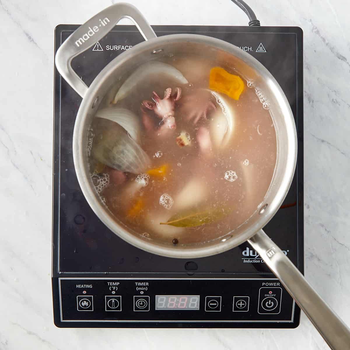 baby octopus being boiled in water with onions, peppers, and spices