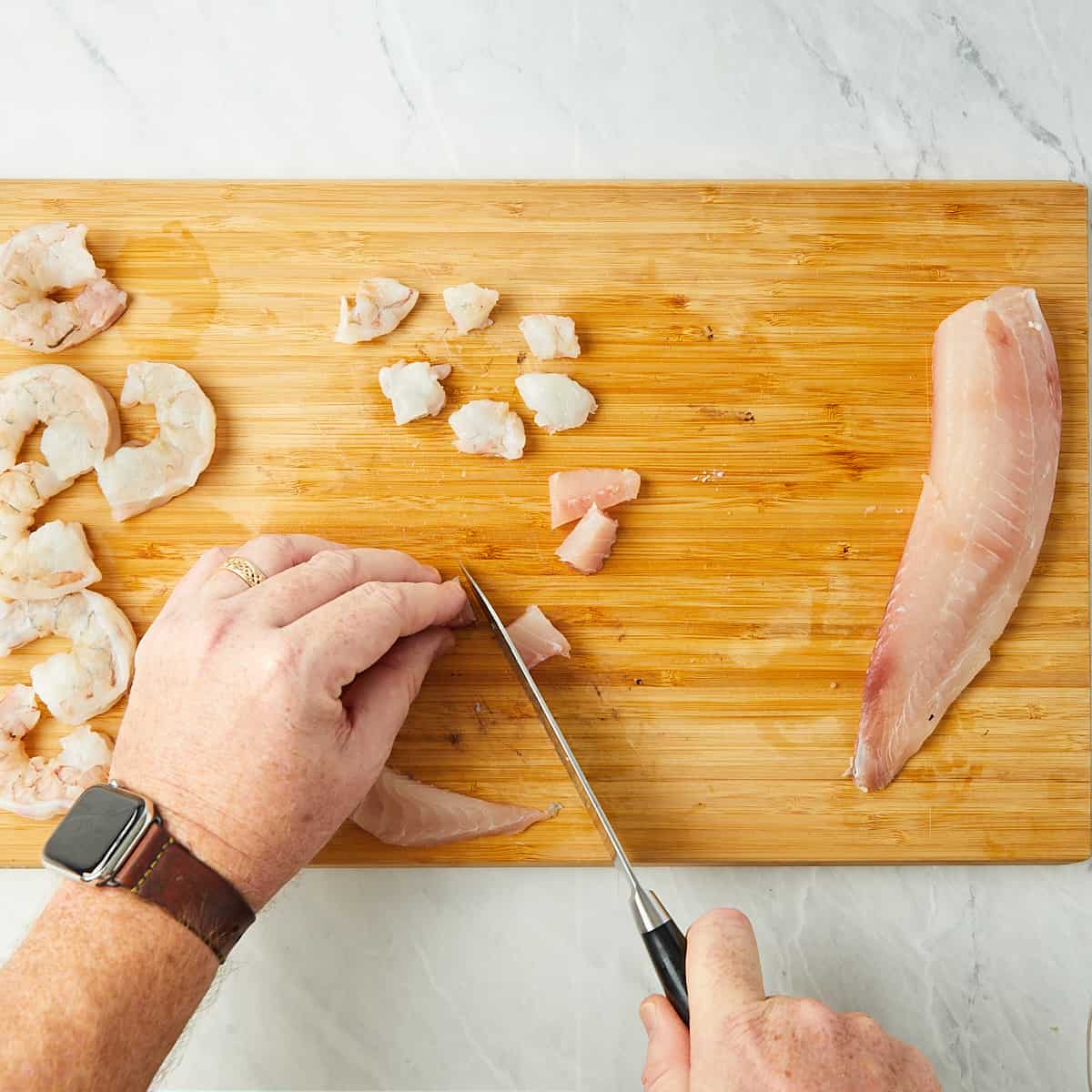 tilapia being cut into 1 inch cubes on a cutting board