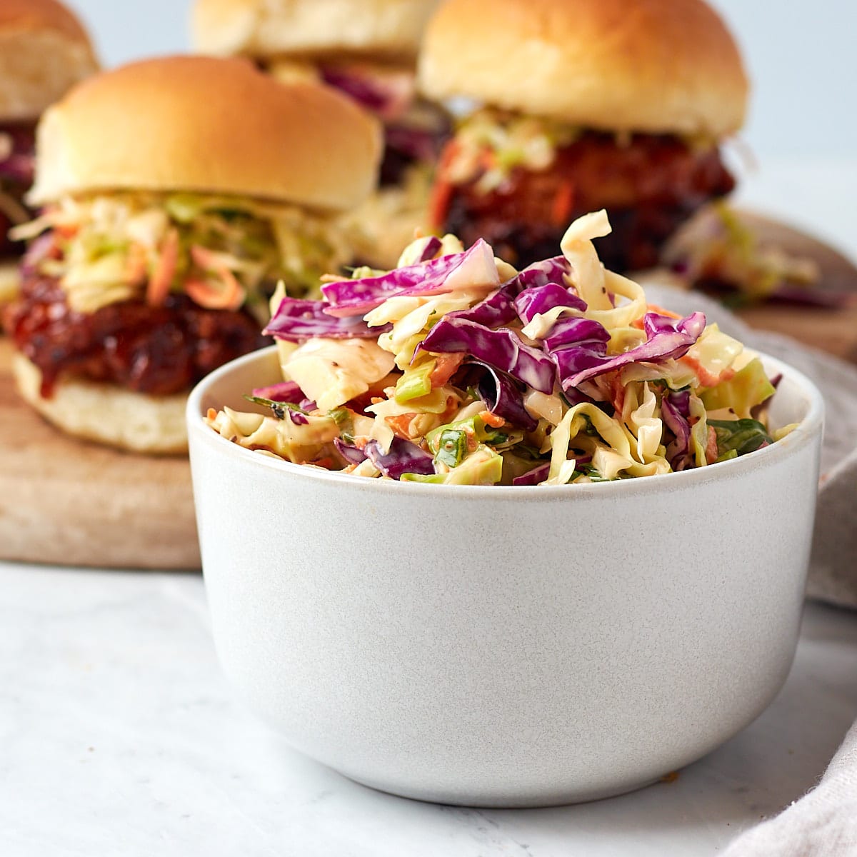 coleslaw in a bowl with chicken sandwiches in the background that were topped with slaw.