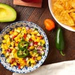 mango salsa in a bowl with a side of chips and a drink.