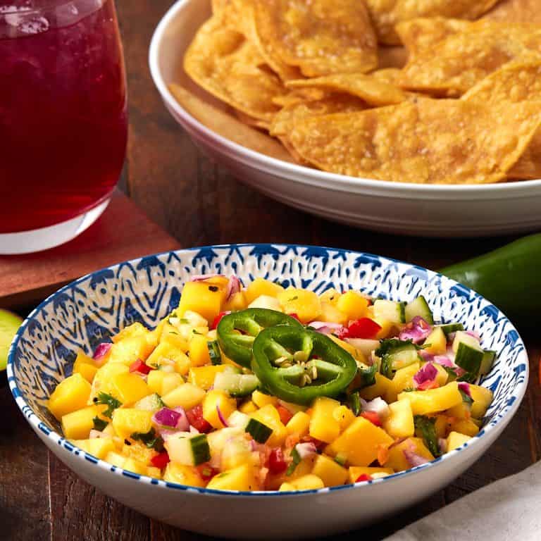 mango salsa in a bowl with a side of chips and a drink.