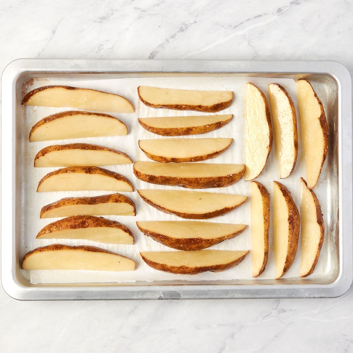 uncooked potato wedges on a cookie sheet.