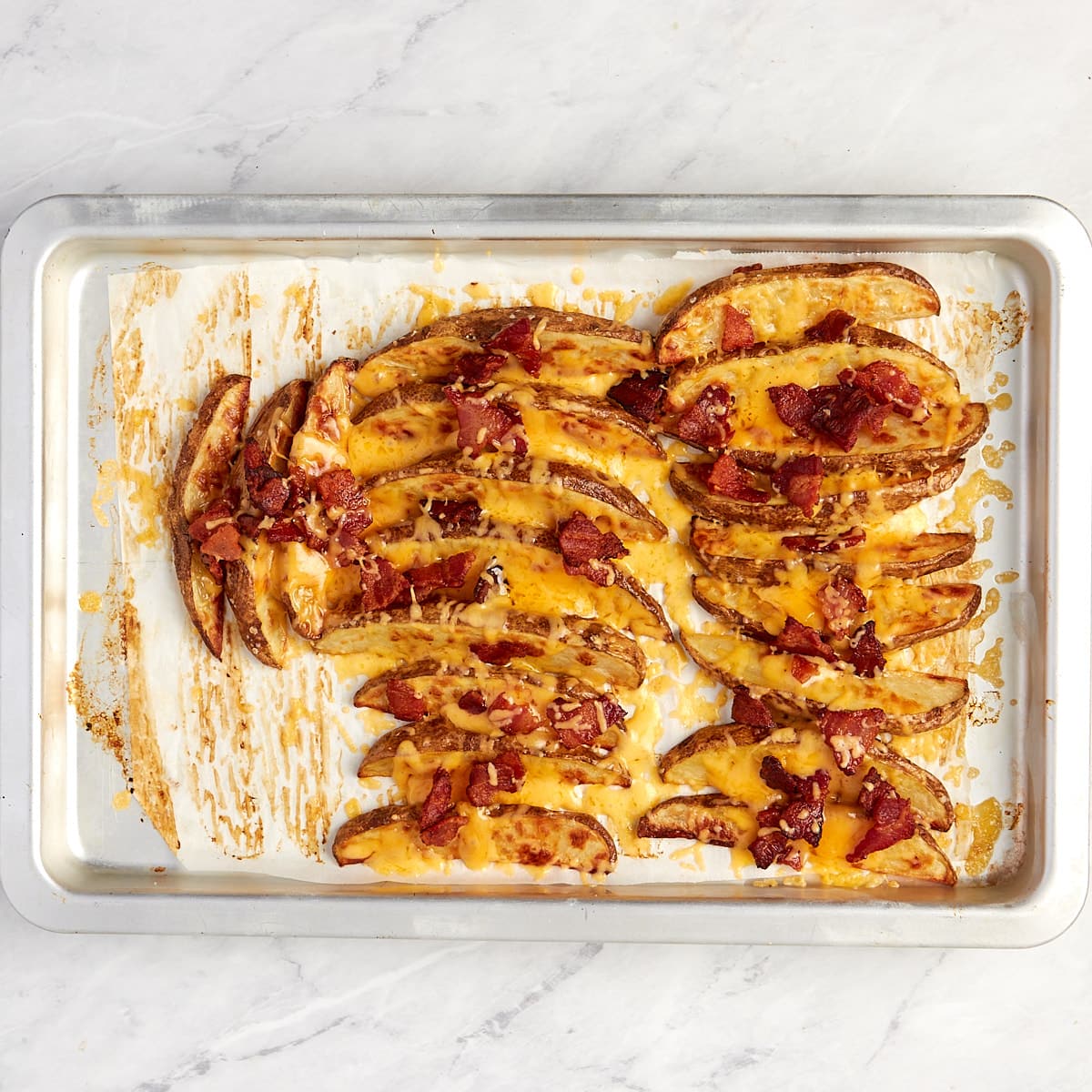 wedges on baking sheet topped with cheese and bacon after being baked.