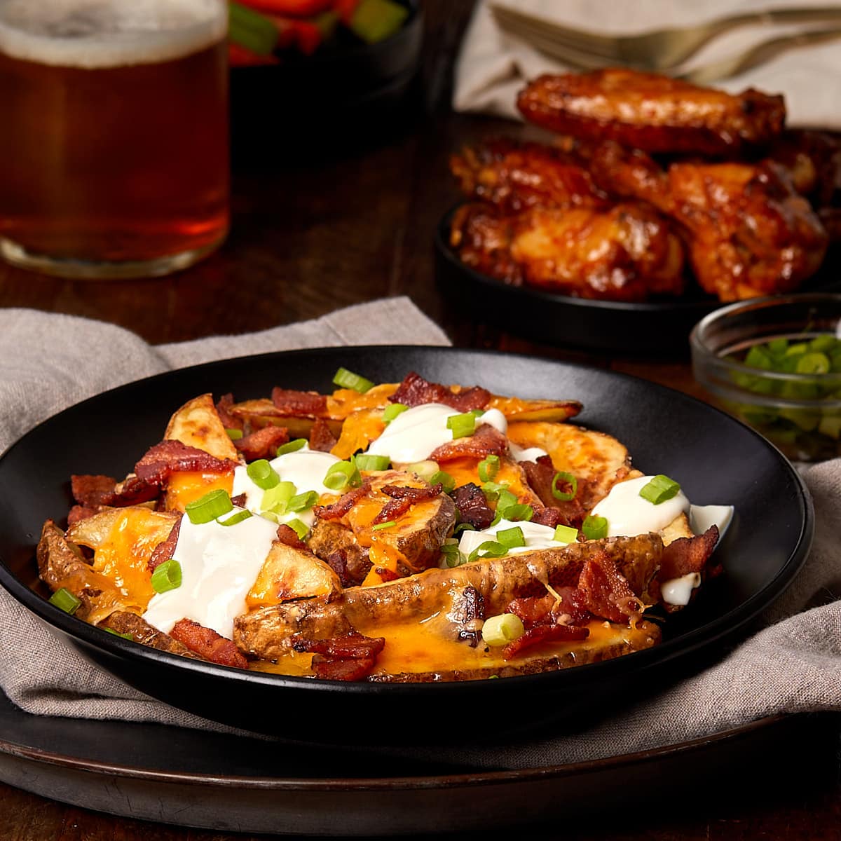 loaded potato wedges in a bowl topped with bacon, cheese, sour cream and chives.