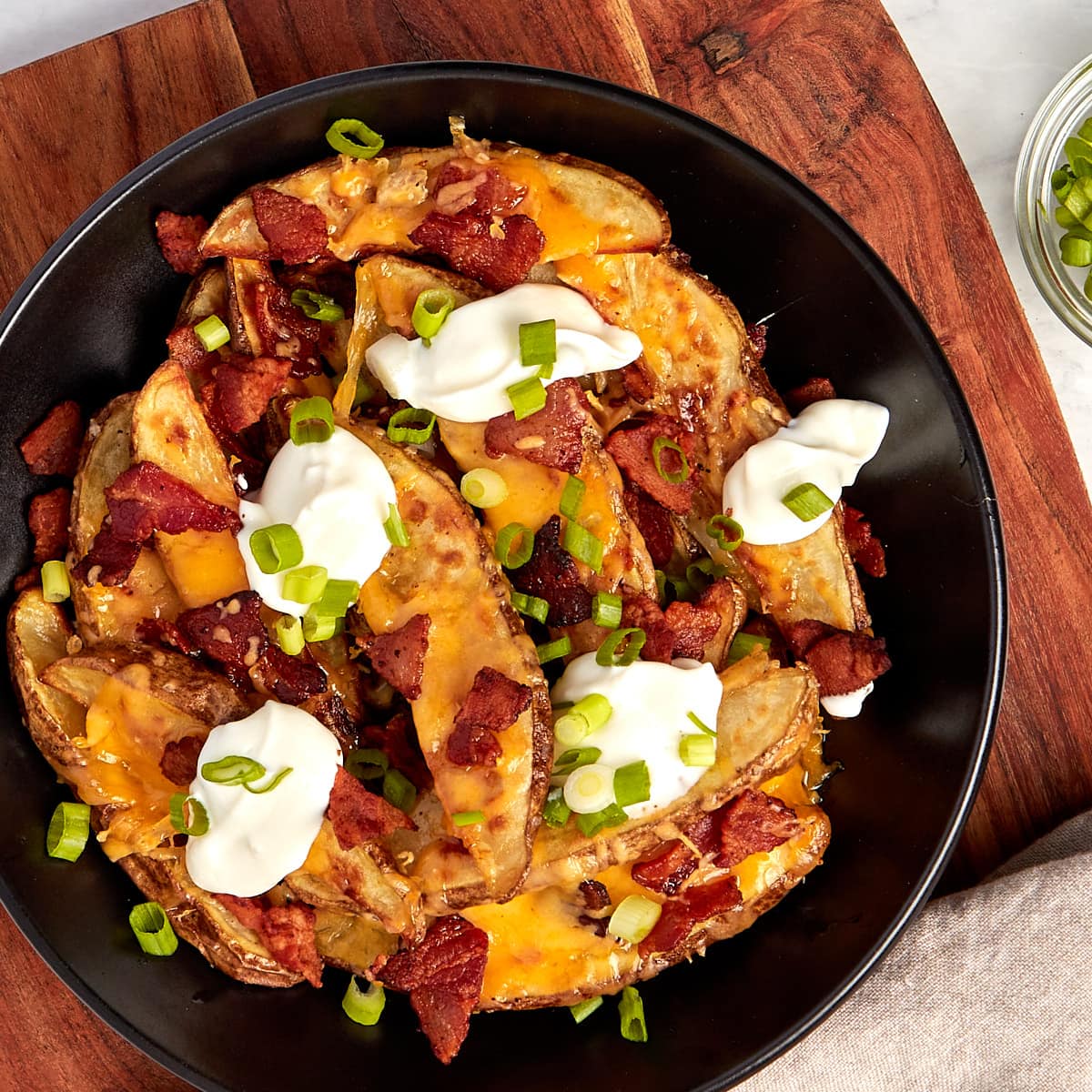 loaded potato wedges in a bowl topped with bacon, cheese, sour cream and chives.
