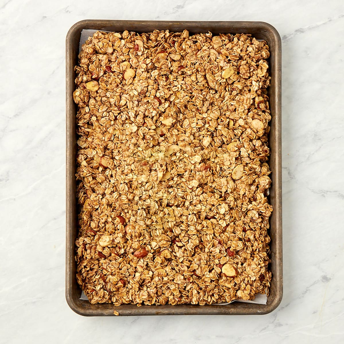 uncooked granola on a cookie sheet spread into an even layer.