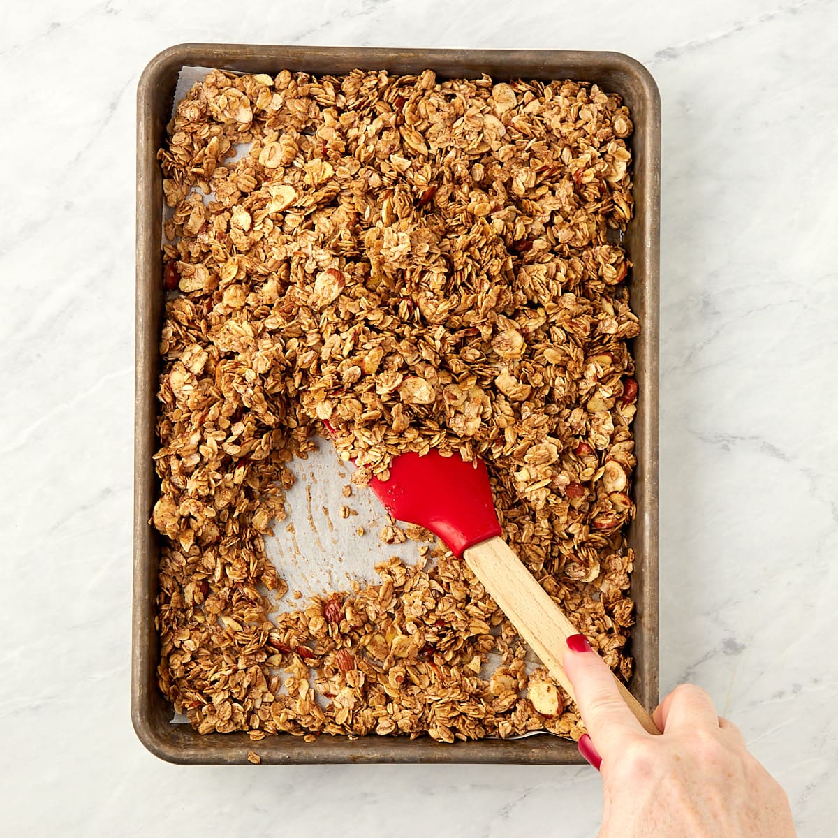 granola on a cookie sheet being stirred.