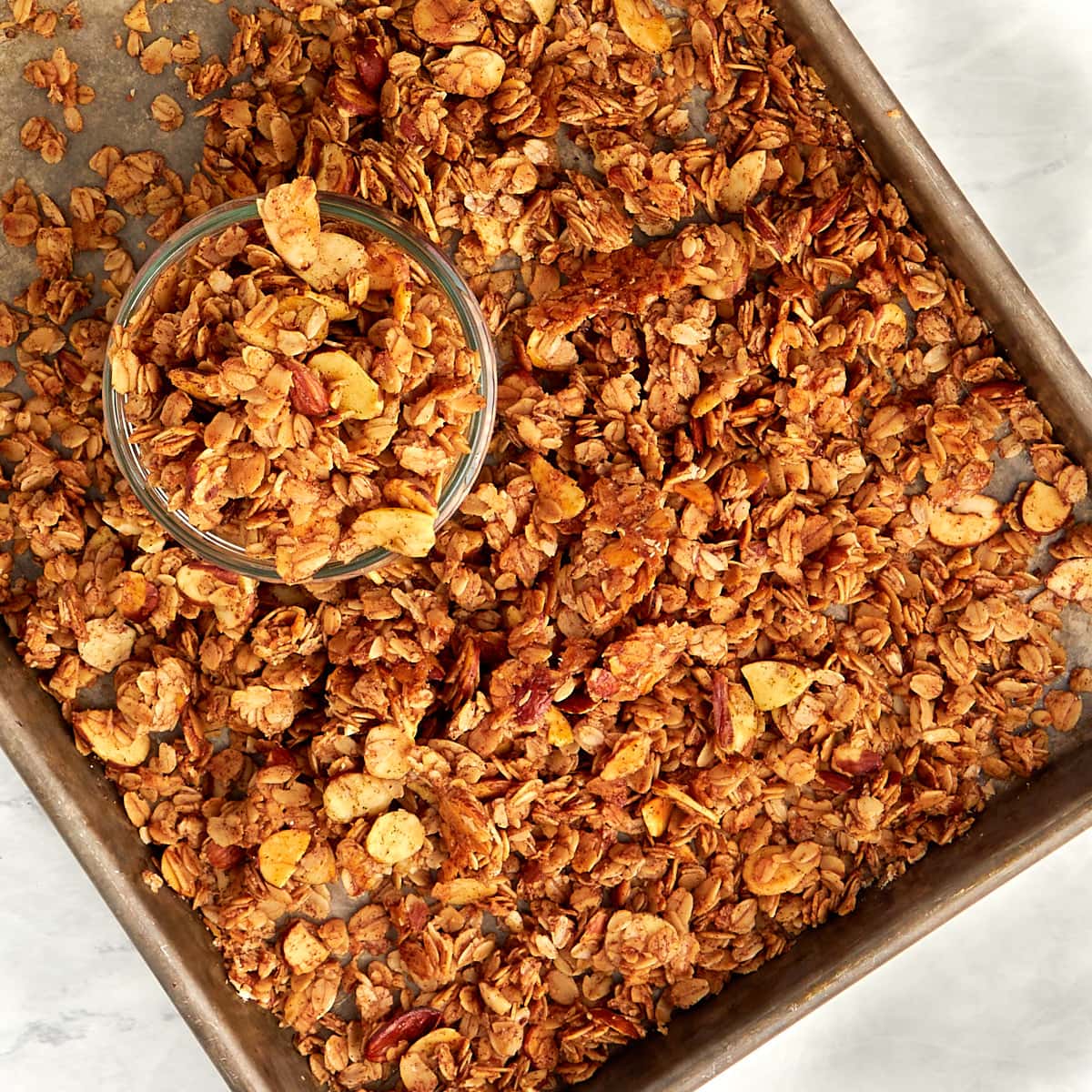 cooked granola on a cookie sheet with some placed in a glass container.