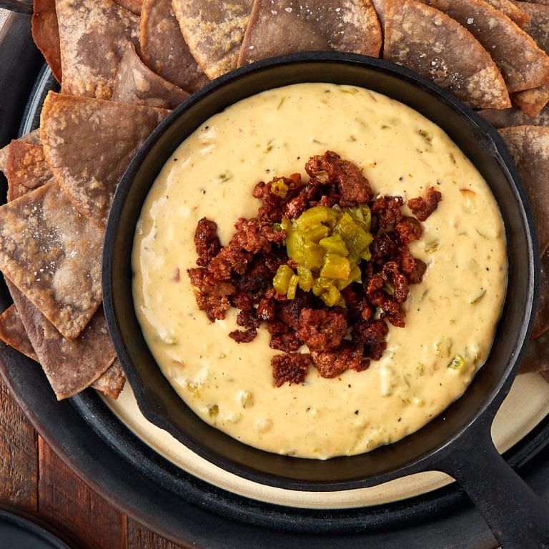hatch queso topped with cooked chorizo in a warm cast iron skillet with a side of tortilla chips.