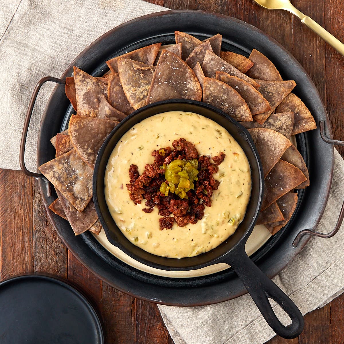 hatch queso topped with cooked chorizo in a warm cast iron skillet with a side of tortilla chips.