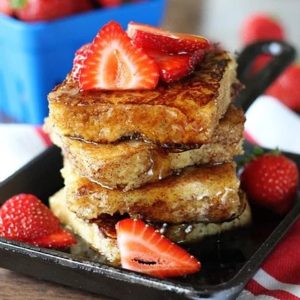stack of cornbread french toast with strawberries and syrup.