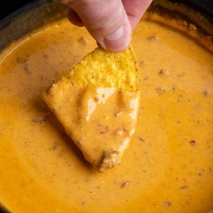 a chip being dipped in chili cheese dip.