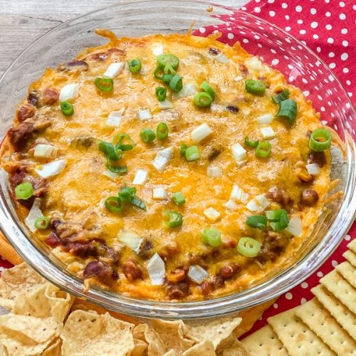 layered chili cheese dip in a bowl with a side of crackers.