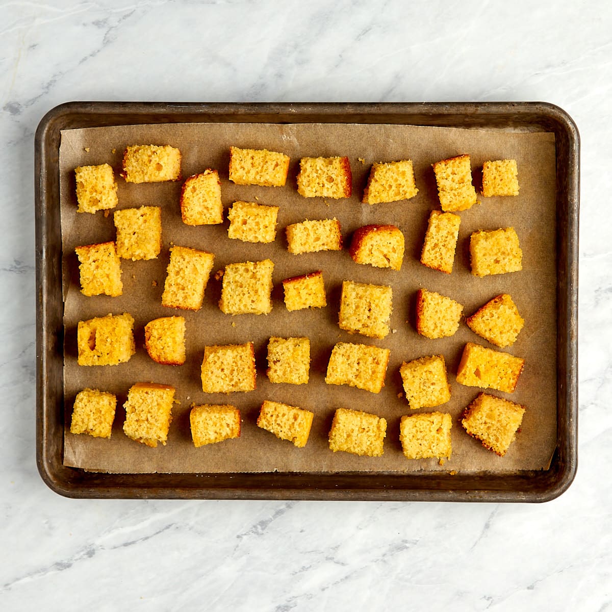 cornbread cubes on a cookie sheet with parchment paper before going into the oven.