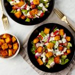 to salads in black bowls topped with salad dressing and croutons.