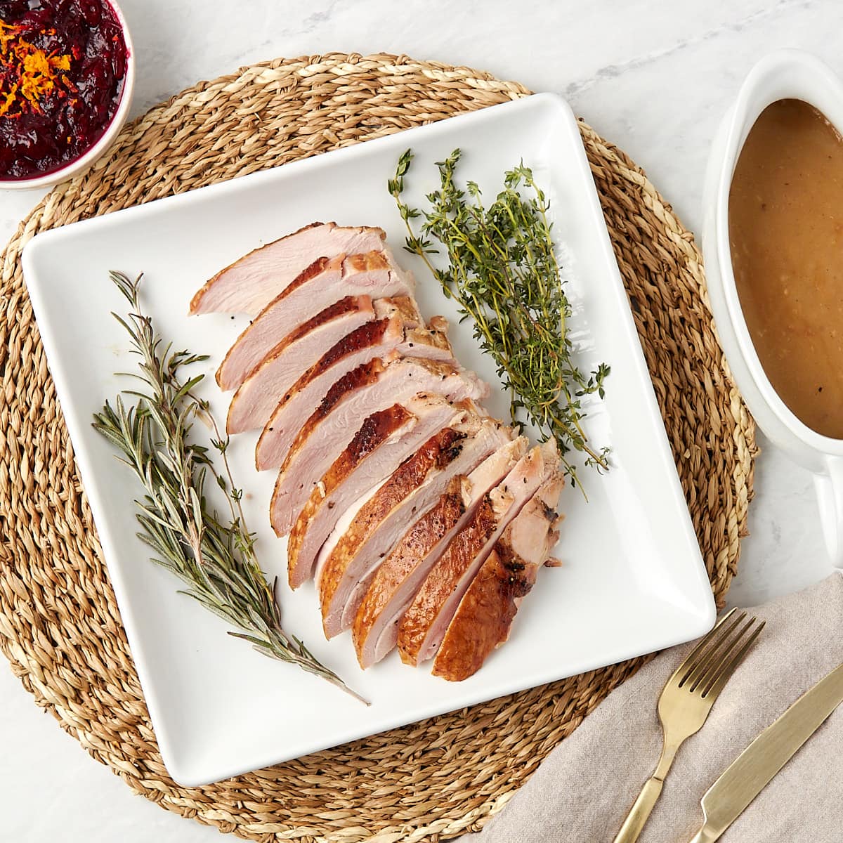 sliced turkey breast on a plate with a side of cranberry sauce and gravy.