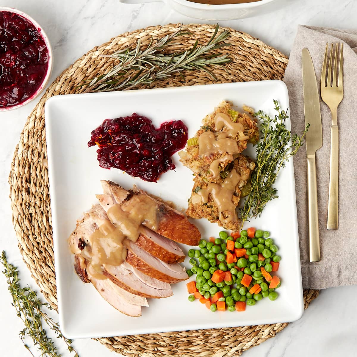 a white plate with a serving of grilled turkey breast and gravy, peas and carrots, thanksgiving dressing, and orange cranberry sauce.