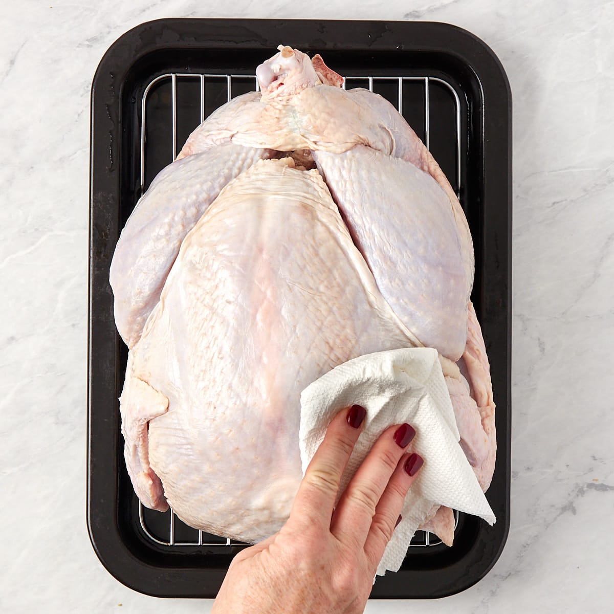 thawed turkey on a wire rack in a pan being patted dry with a paper towel.