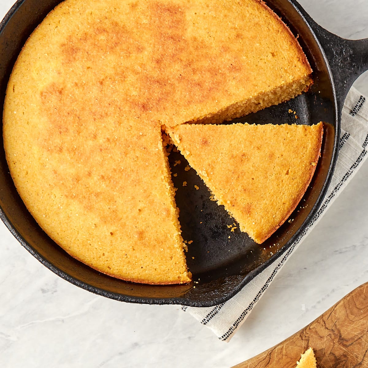 cooked cornbread in a cast iron skillet with a slice cut out.