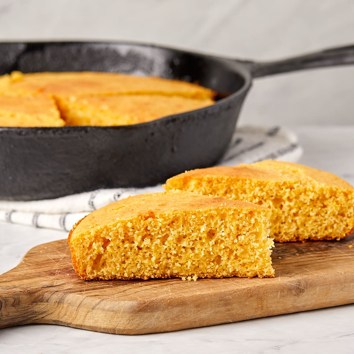 two slices of cornbread on a small wooden cutting board.