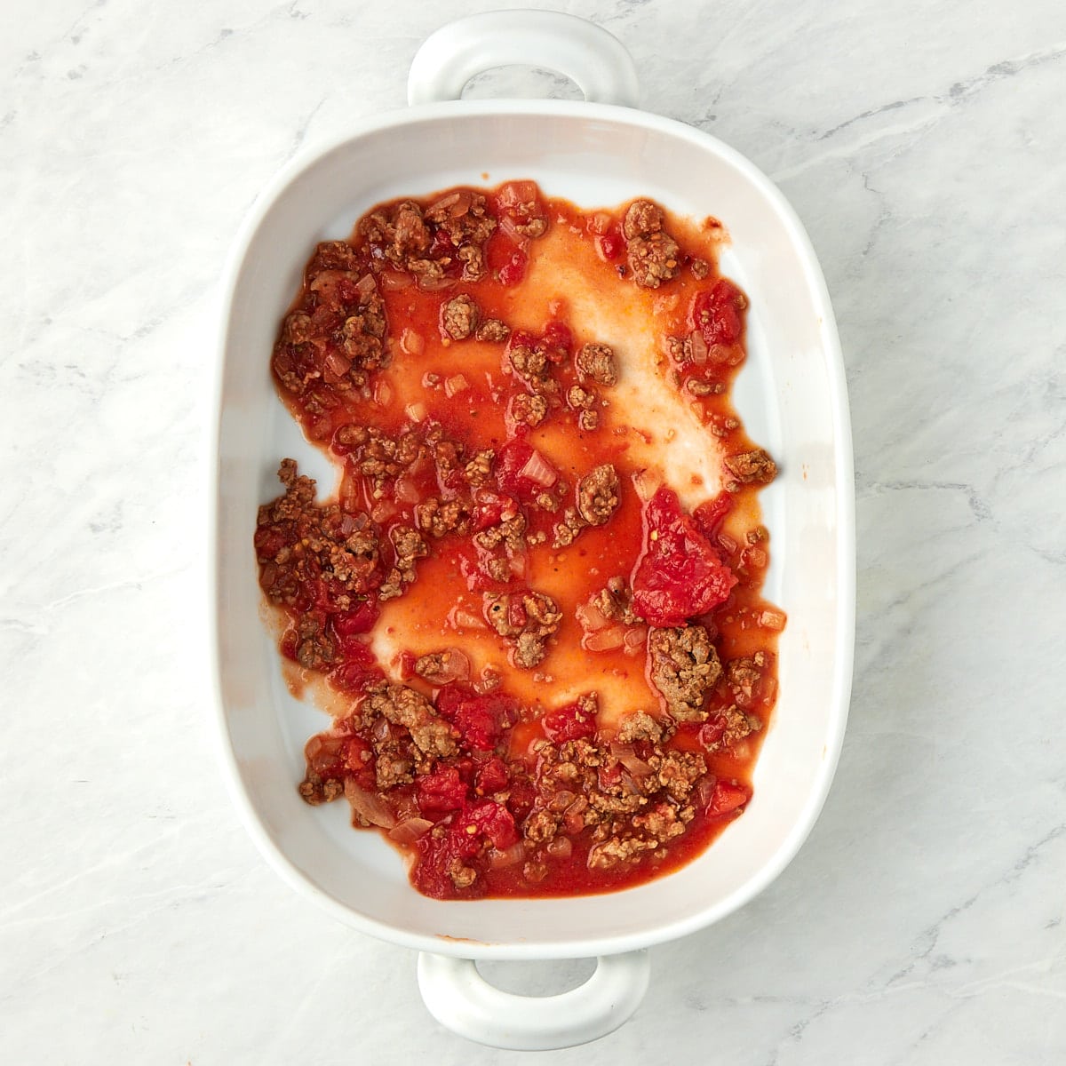 a layer of meat sauce in a casserole dish.