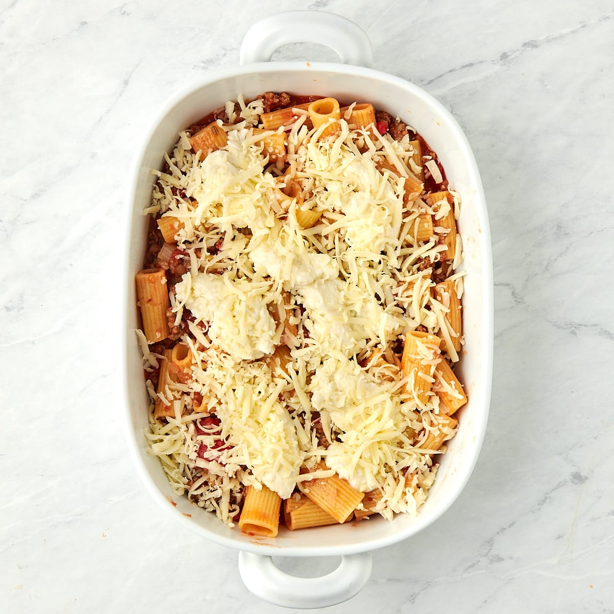 pasta and meat sauce in a casserole dish with dollops of ricotta and shredded mozzarella.
