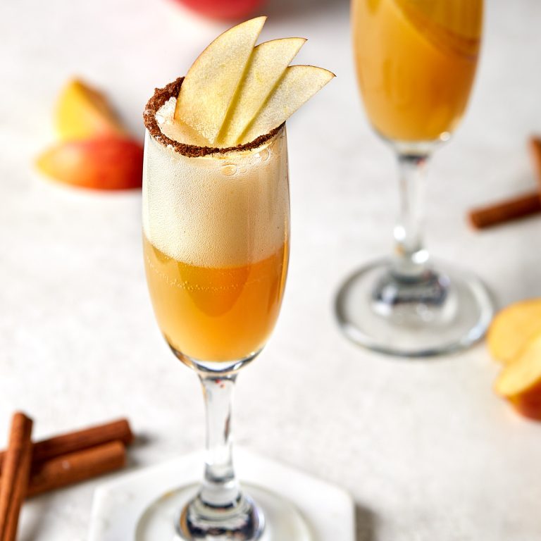 apple cider mimosa in champagne flutes with apple garnish and a cinnamon sugared rim.