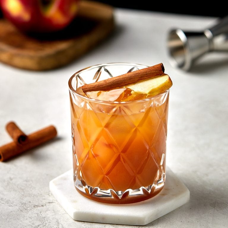 whiskey sour garnished with a cinnamon stick and apple slice.