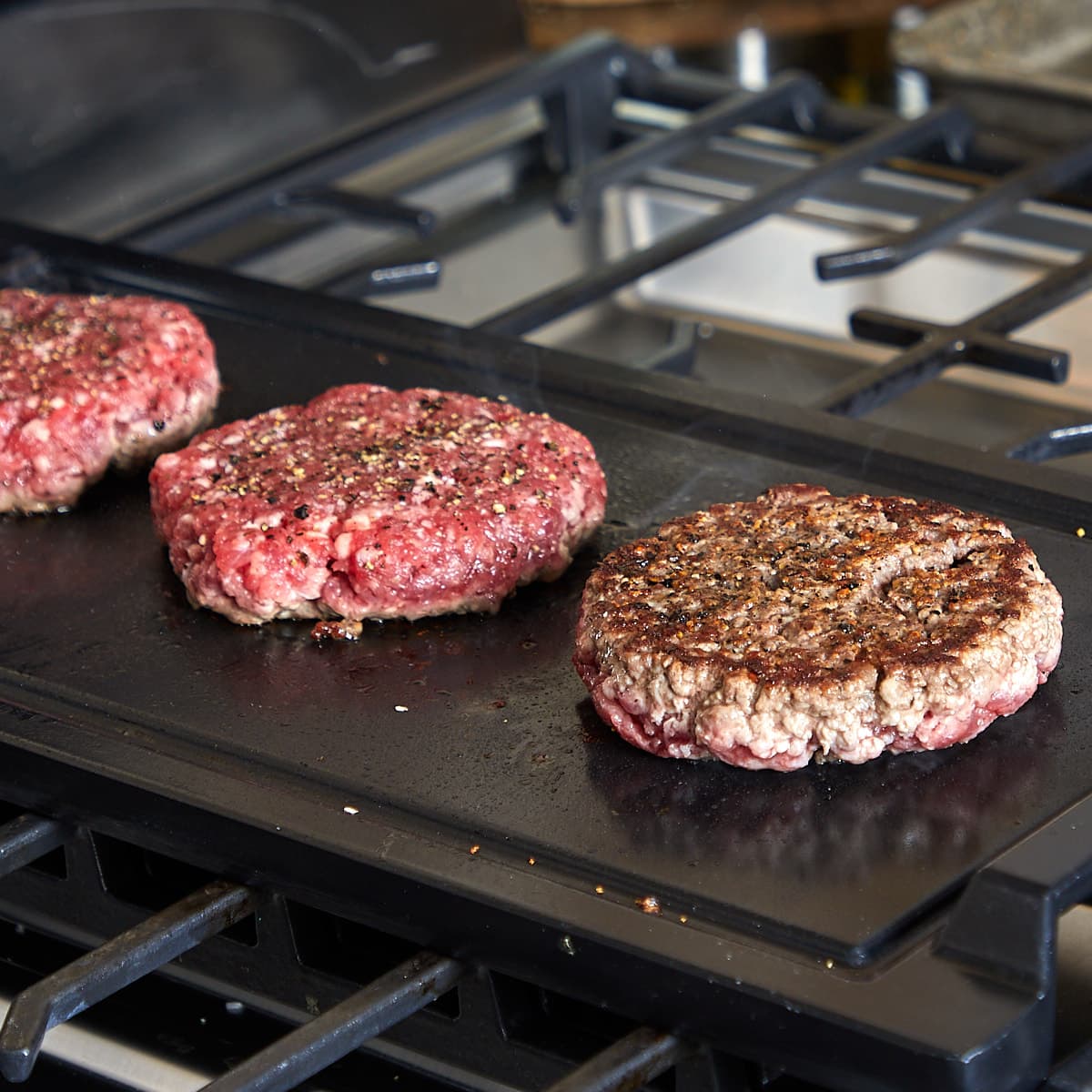 three hamburger patties grilling on a flat top with one of them flipped over and cooking on the other side.