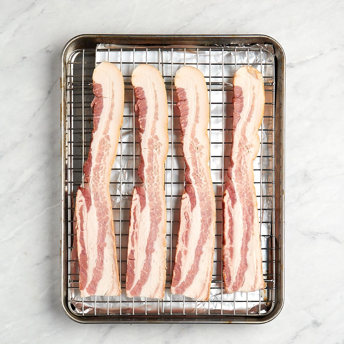 uncooked bacon on a wire rack in a baking sheet.