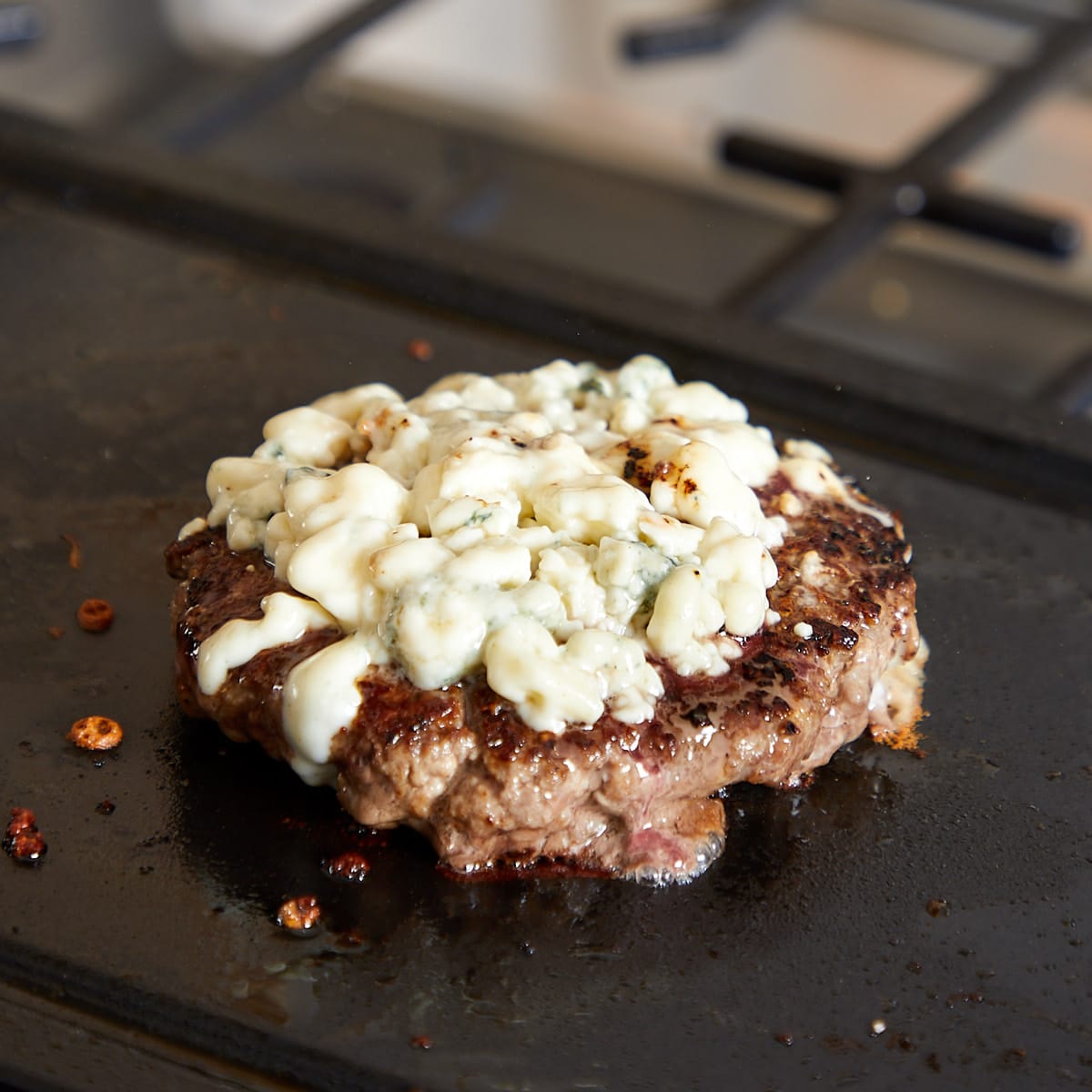 burger patty topped with blue cheese on a flat top top grill.